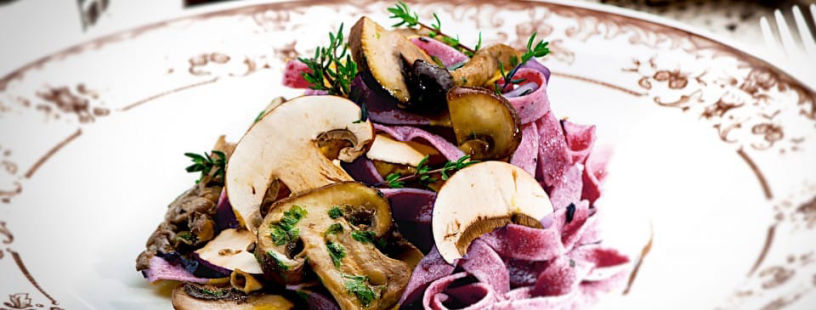 Purple pasta with sautéed mushrooms and fresh herbs on white plate
