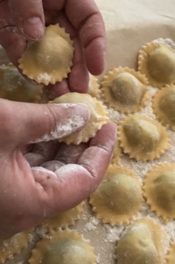 Hands shaping fresh ravioli pasta on floured marble surface